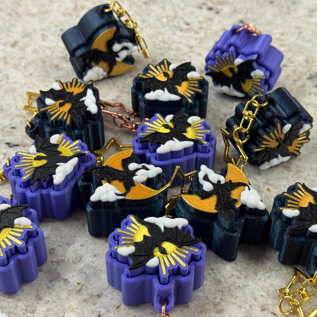 Collection of fidget clicker keychains in dark blue or purple with a dragon flying front of either a moon or sunburst