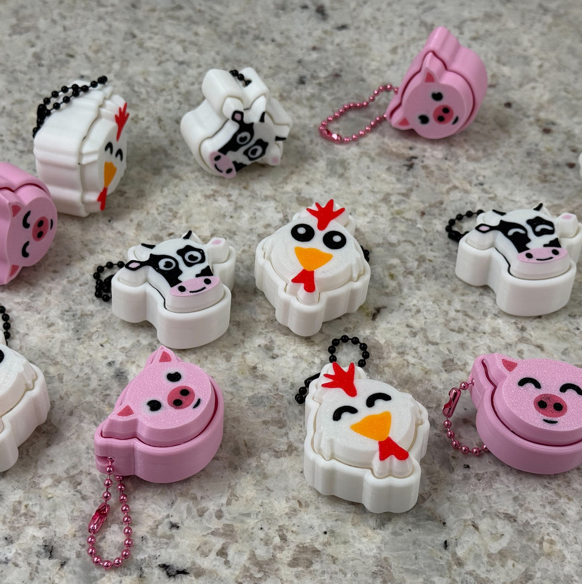 Collection of cartoon animal-themed fidget clickers on a textured surface. Animals include cows, pigs, and chickens.