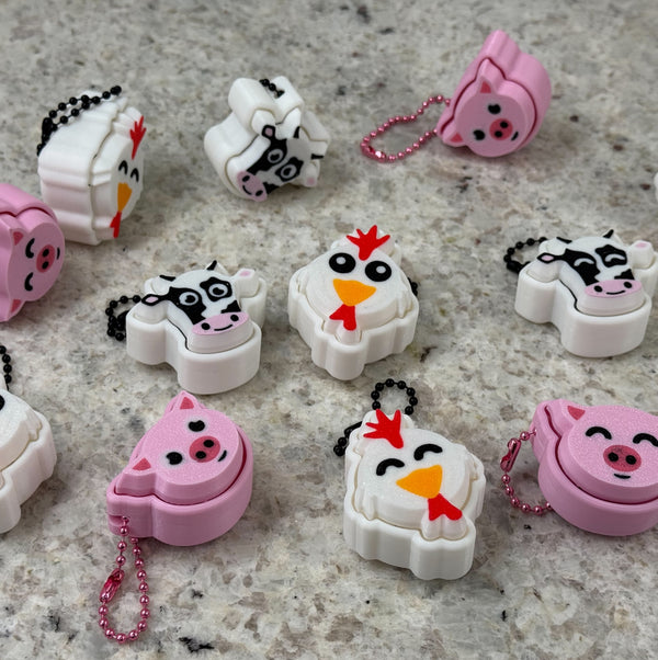 Collection of cartoon animal-themed fidget clickers on a textured surface. Animals include cows, pigs, and chickens.