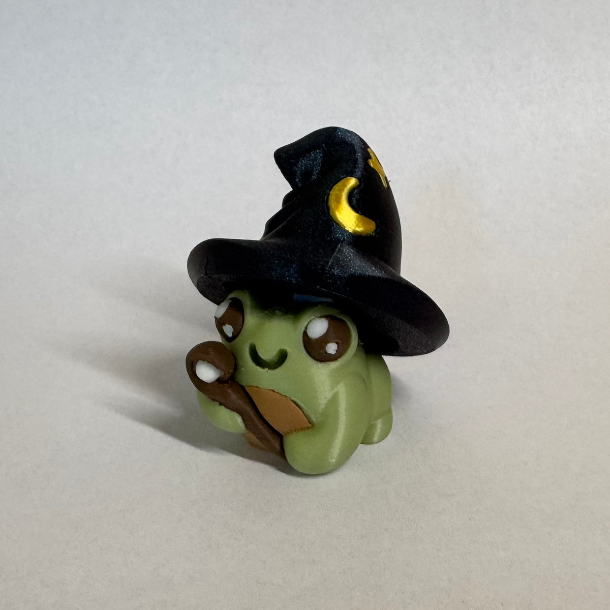 Small green frog fidget clicker dressed up as a wizard with a wand and a pointy hat with stars and a moon on it