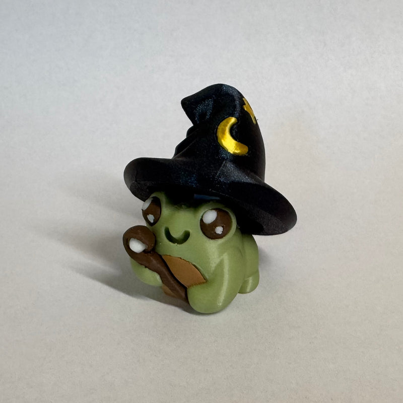 Small green frog fidget clicker dressed up as a wizard with a wand and a pointy hat with stars and a moon on it