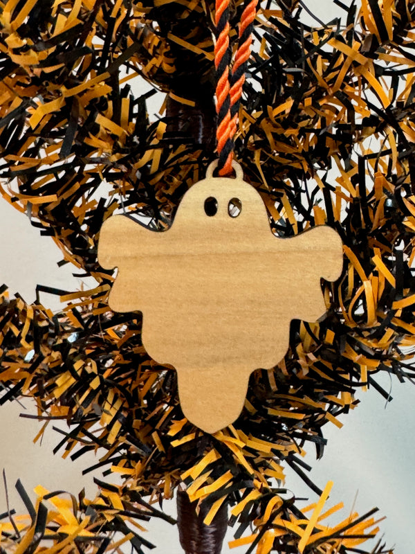 Wooden ghost ornament hanging on a black and orange tree